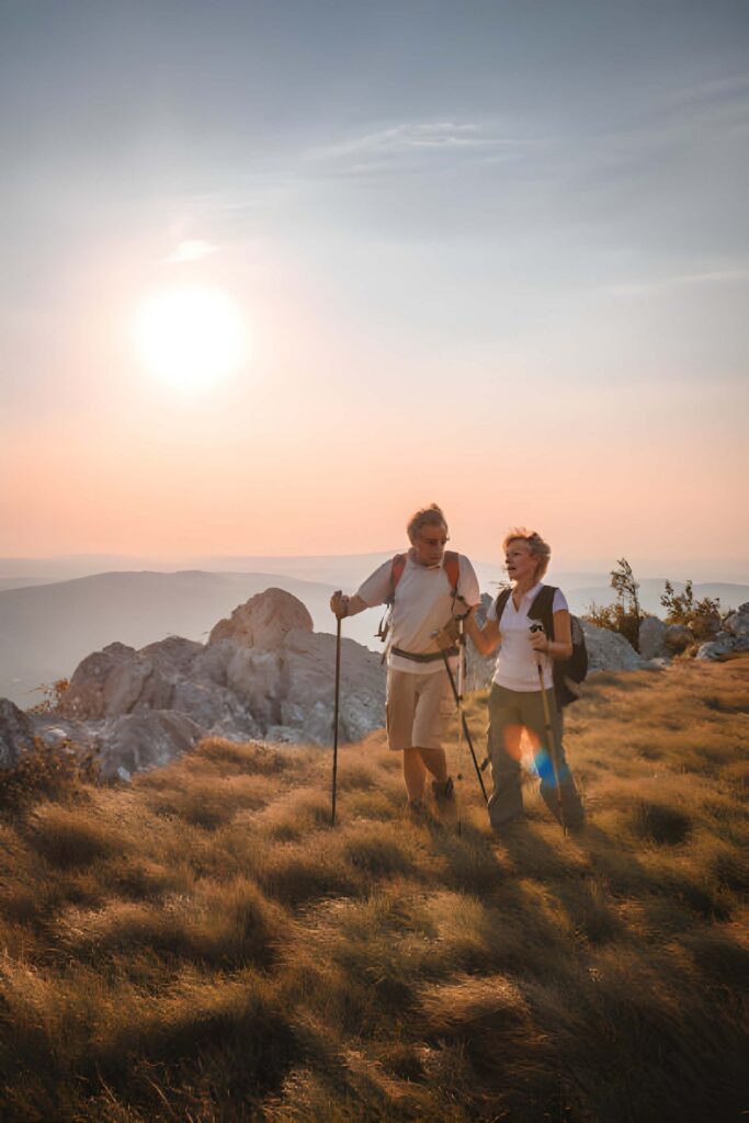 Two hikers walking on grassy ridge at sunset