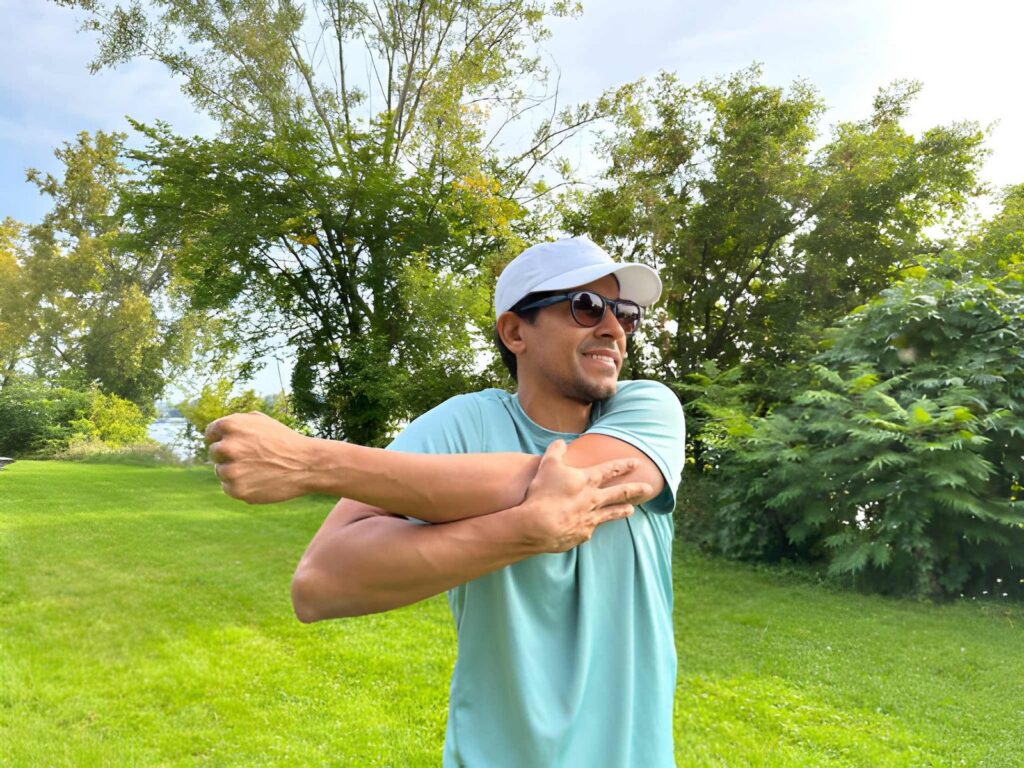 Person stretching outdoors wearing cap and sunglasses