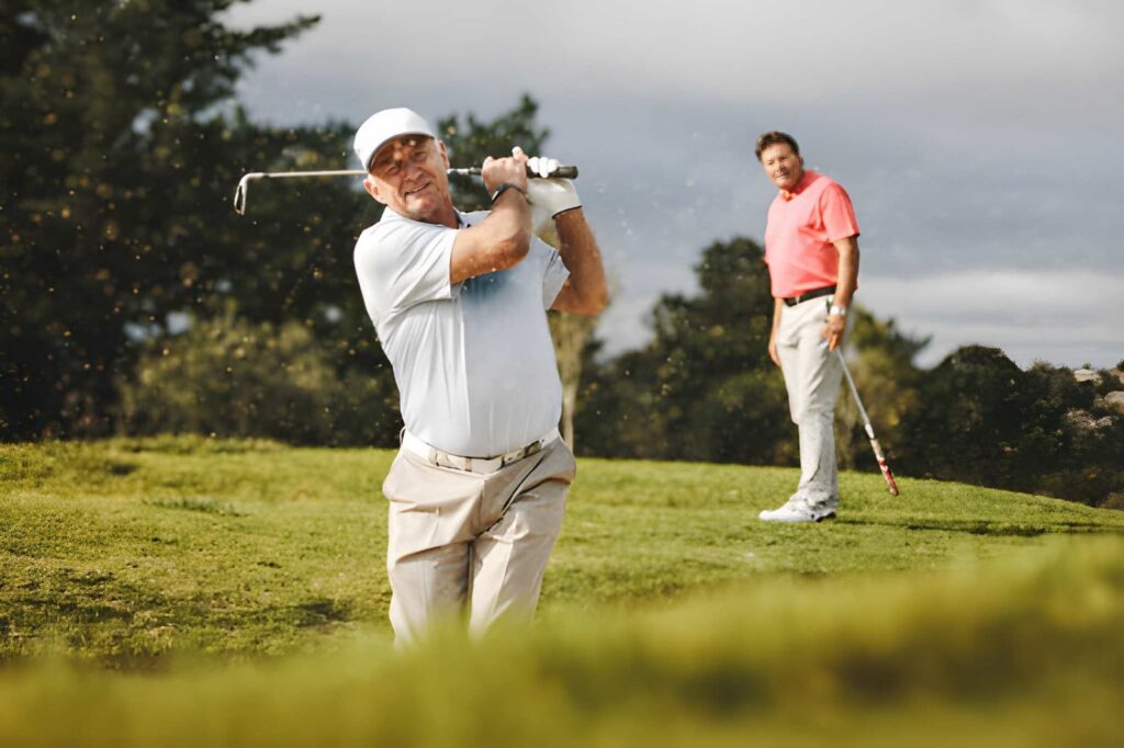 Man swinging golf club while companion watches