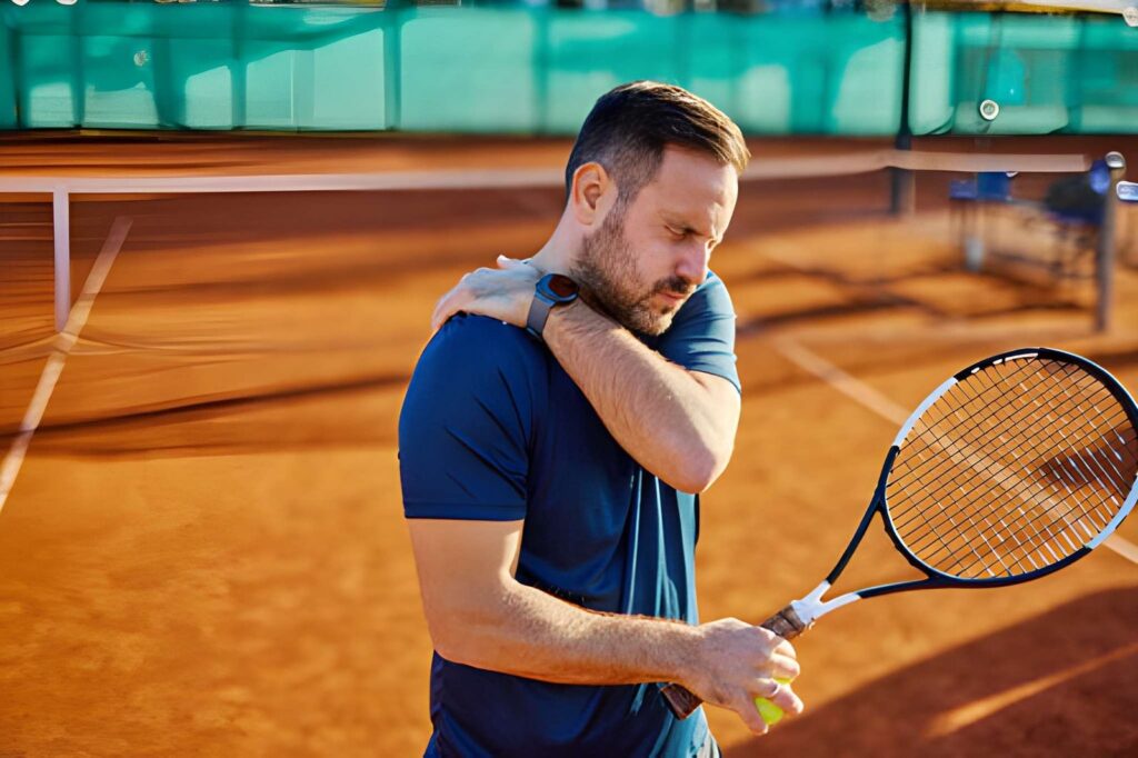 Tennis player clutching shoulder on clay court