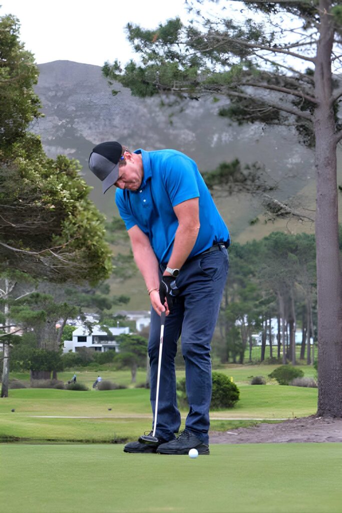 Golfer putting on green with mountain backdrop