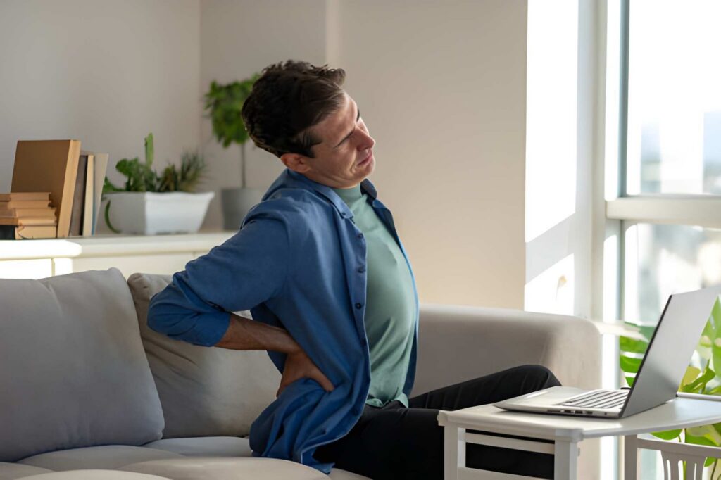 Man holding lower back while working on laptop