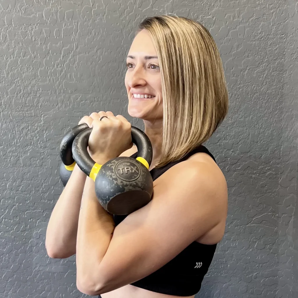 Smiling woman holding kettlebells at chest